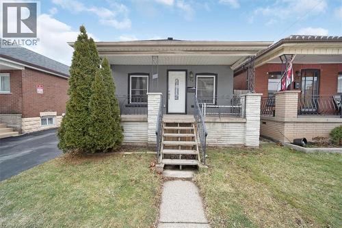 Grey exterior with white trim, featuring a covered porch with decorative railing and a white entry door - 106 Lottridge Street, Hamilton, ON 