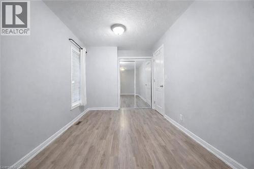 Spacious room with wood-finish flooring, white baseboards, and light gray walls - 106 Lottridge Street, Hamilton, ON 