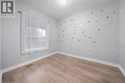 Room featuring wood-finish flooring, a window with a sheer curtain, and light grey walls - 106 Lottridge Street, Hamilton, ON 