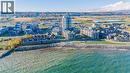 Coastal community featuring a prominent high-rise building and various lower-rise residential structures, situated alongside a rocky shoreline - 40 Esplanade Lane Unit# 614, Grimsby, ON 