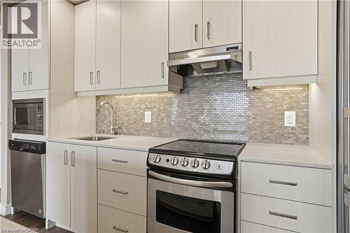 Modern kitchen featuring light wood-finish cabinetry, stainless steel appliances, a tile mosaic backsplash, under-cabinet lighting, and light-toned countertops - 40 Esplanade Lane Unit# 614, Grimsby, ON 