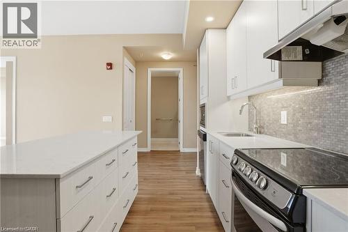 Modern kitchen featuring a white countertop island, white cabinetry, a built-in range, a stainless steel sink, and a gray tile backsplash - 40 Esplanade Lane Unit# 614, Grimsby, ON 