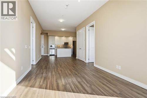 Open-concept living area featuring wood-finish flooring, a kitchen with white cabinetry, stainless steel appliances, and a breakfast bar - 40 Esplanade Lane Unit# 614, Grimsby, ON 
