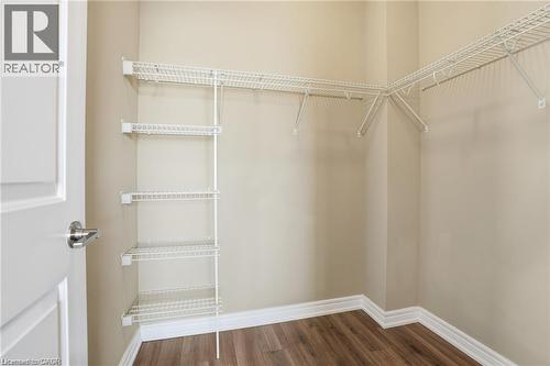 Walk-in closet featuring wood-finish flooring, white wire shelving, wall-mounted racks, beige wall paint, and white baseboards - 40 Esplanade Lane Unit# 614, Grimsby, ON 