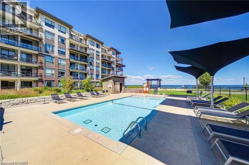 Outdoor swimming pool with concrete surround, shaded lounge areas, and a multi-story building featuring private balconies - 40 Esplanade Lane Unit# 614, Grimsby, ON 