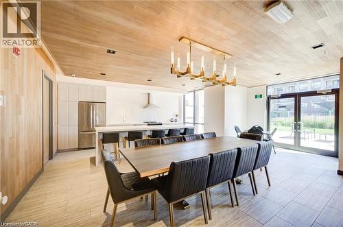 Modern dining area featuring a large rectangular table with seating for eight, illuminated by a contemporary gold-finish chandelier - 40 Esplanade Lane Unit# 614, Grimsby, ON 