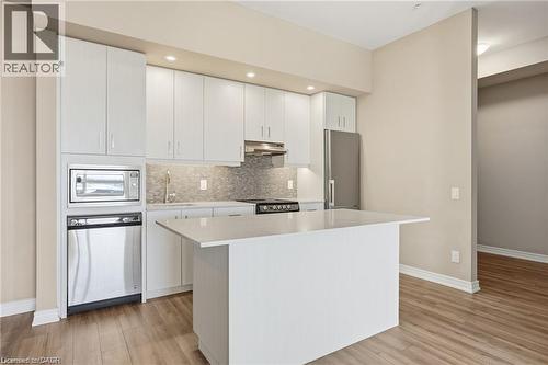 Contemporary kitchen featuring white cabinetry, a large center island, stainless steel appliances, and wood-finish flooring - 40 Esplanade Lane Unit# 614, Grimsby, ON 
