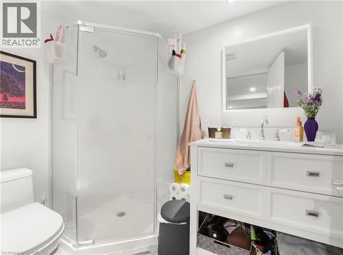 Modern basement bathroom featuring a glass-enclosed shower with a chrome showerhead, a white toilet, and a white vanity with an integrated sink and chrome fixtures - 420 Waverly Street, Hamilton, ON 