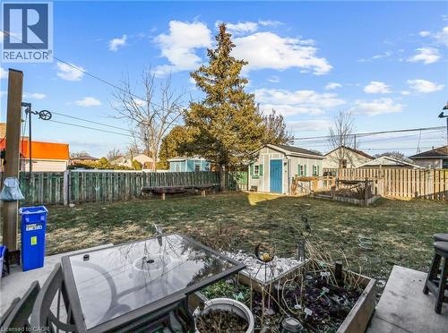 Expansive backyard featuring a manicured lawn, a detached storage shed with a blue door and green shutters, and a wooden privacy fence - 420 Waverly Street, Hamilton, ON 