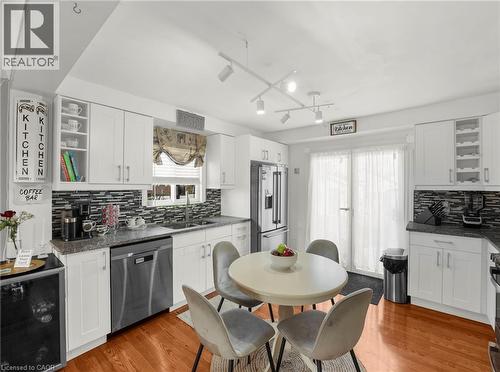 Kitchen featuring white cabinetry, wood-finish flooring, a mosaic tile backsplash, stainless steel appliances, and a glass-paneled exterior door. Some virtual staging - 420 Waverly Street, Hamilton, ON 