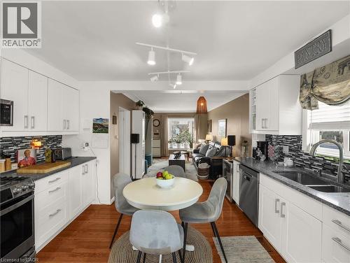 Bright kitchen featuring white cabinetry, granite-style countertops, mosaic tile backsplash, and wood-finish flooring - 420 Waverly Street, Hamilton, ON 