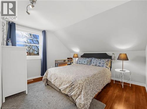 Bedroom featuring sloped ceilings, hardwood flooring, and a large window with blue drapes - 420 Waverly Street, Hamilton, ON 