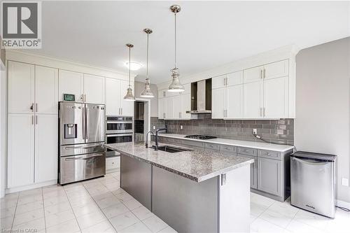 Contemporary kitchen featuring a large central island with a sink, stainless steel appliances, white cabinetry, a gray subway tile backsplash, and light-toned tile flooring - 417 Rivertrail Avenue, Kitchener, ON 