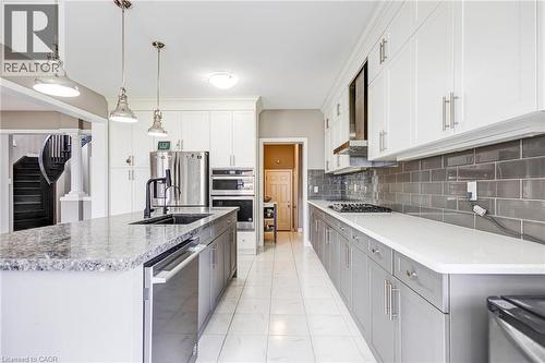 Gourmet kitchen featuring a large island with a stone countertop, a built-in sink with a black faucet, and stainless steel appliances - 417 Rivertrail Avenue, Kitchener, ON 
