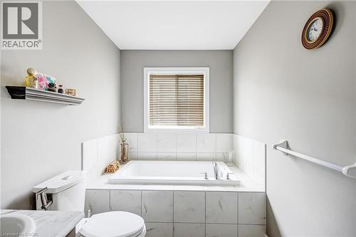 Soaking tub with a tiled surround, window with blinds, and light-colored walls - 417 Rivertrail Avenue, Kitchener, ON 
