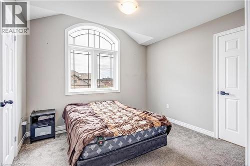 Arched window with decorative grilles, light gray painted walls, textured gray carpeting, white trim, and white panel doors with black hardware - 417 Rivertrail Avenue, Kitchener, ON 