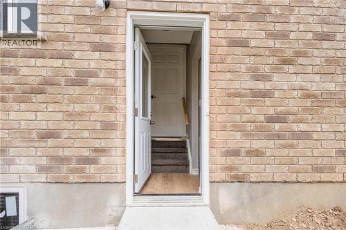Brick exterior with a white storm door, leading to interior stairs with wood-finish flooring and a paneled door - 417 Rivertrail Avenue, Kitchener, ON 