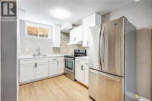 Kitchen featuring white shaker-style cabinetry, stainless steel appliances, light wood-finish flooring, a white subway tile backsplash, and a contemporary sink with a gooseneck faucet - 417 Rivertrail Avenue, Kitchener, ON 