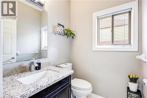 Bathroom featuring a vanity with a light-toned speckled countertop and undermount sink, a chrome faucet, a rectangular mirror, and a window with blinds - 417 Rivertrail Avenue, Kitchener, ON 