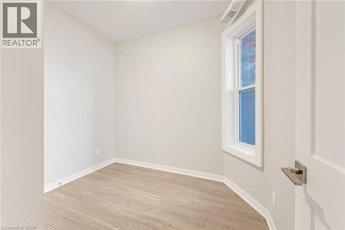 Room featuring wood-finish flooring, crisp white baseboards, a white-framed window, neutral wall tones, and a paneled interior door with a brushed nickel lever - 657 Barton Street E Unit# 302, Hamilton, ON 