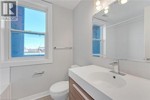 Modern bathroom featuring a single window, a floating vanity with integrated sink, a chrome faucet, a large frameless mirror, and overhead vanity lighting - 657 Barton Street E Unit# 302, Hamilton, ON 