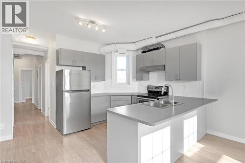 Contemporary kitchen featuring light gray cabinetry, stainless steel appliances, a double basin sink, and a contrasting light speckled countertop - 657 Barton Street E Unit# 302, Hamilton, ON 