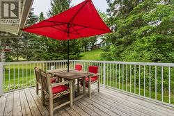 Expansive wood deck with white railings, offering views of a sloped lawn and mature trees - 