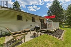 Backyard featuring a raised wooden deck with white railing, sliding glass door access, an adjacent concrete patio, and mature evergreen trees - 
