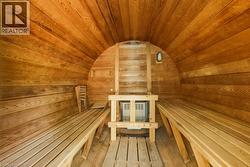 Barrel sauna with light wood-finish walls and ceiling, featuring two built-in benches, a central heater, and a wall-mounted light fixture - 