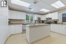 Functional kitchen featuring white cabinetry, light-toned countertops, a central island with an integrated sink, a large window, and recessed ceiling lighting - 