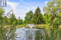 Serene pond with an active fountain, surrounded by lush green foliage and mature trees - 