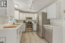 U-shaped kitchen featuring white cabinetry, light countertops, wood-finish flooring, a stainless steel appliance suite, and a track lighting fixture - 