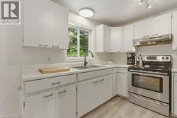 Kitchen featuring white cabinetry, light-toned countertops, a stainless steel range with overhead hood, a double basin sink, and wood-finish flooring - 