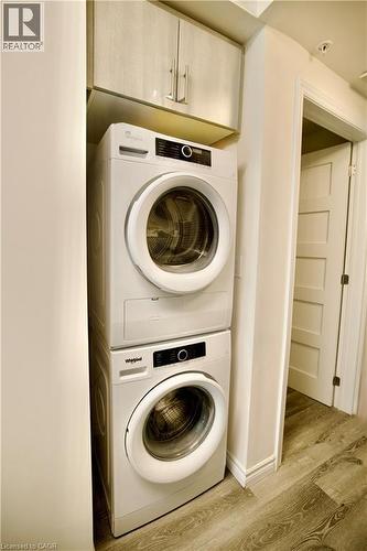 Laundry area featuring a stacked washer and dryer, upper cabinetry with light wood-finish doors, and wood-finish flooring - 246 Lester Street Unit# 306, Waterloo, ON 