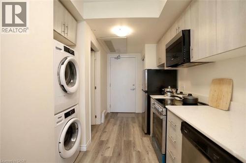 Galley kitchen with stacked laundry appliances featuring wood-finish flooring, white countertops, light wood-finish cabinetry, and stainless steel appliances - 246 Lester Street Unit# 306, Waterloo, ON 