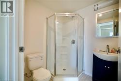 Compact bathroom featuring a corner shower with glass enclosure, single vanity with dark blue cabinetry, wall-mounted mirror, and tile flooring - 