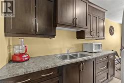 Kitchen featuring dark wood cabinetry with brushed nickel hardware, a double basin stainless steel sink, and speckled grey countertops - 