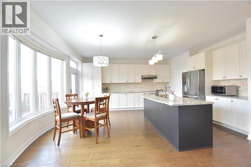 Two tone kitchen with stainless steel appliances, an island with sink, light stone counters, hanging light fixtures, and dark wood-style floors - 512 Terrington Crescent, Kitchener, ON 