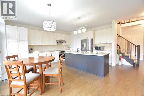 Two tone kitchen featuring stainless steel appliances, a kitchen island with sink, decorative backsplash, light stone counters, and dark wood-style flooring - 512 Terrington Crescent, Kitchener, ON 