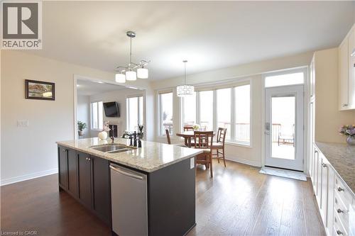 Kitchen featuring light stone countertops, stainless steel dishwasher, an island with sink, hanging light fixtures, and dark wood finished floors - 512 Terrington Crescent, Kitchener, ON 