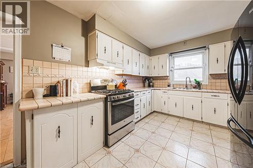 Kitchen featuring white cabinetry with dark hardware, a stainless steel range, and a dual-basin sink under a window - 70 Webster Road, Hamilton, ON 