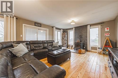 Spacious living area featuring wood-finish flooring, a wood-burning stove with a stone accent wall, and multiple large windows - 70 Webster Road, Hamilton, ON 