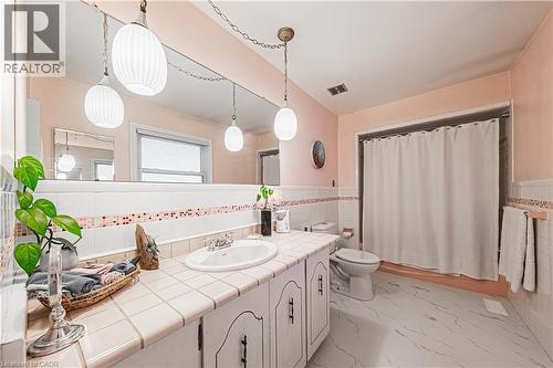Bathroom featuring a white tiled vanity with an integrated sink, a large wall-mounted mirror, and pendant lighting - 70 Webster Road, Hamilton, ON 