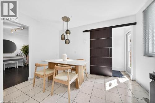 Dining space featuring a modern pendant light fixture, light-toned tile flooring, and a dark wood-finish barn door - 19 Glen Forest Drive, Hamilton, ON 