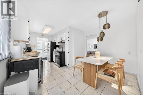 Kitchen and dining area featuring white cabinetry, tile flooring, and a contemporary pendant light fixture - 19 Glen Forest Drive, Hamilton, ON 