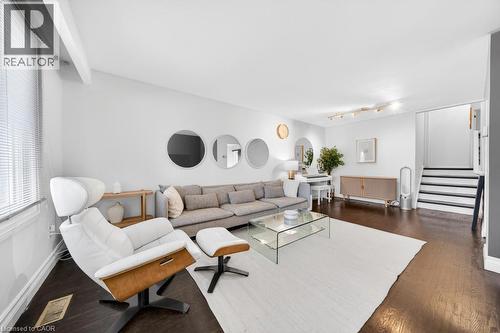 Bright living area featuring dark wood-finish flooring, white walls, and a staircase with dark treads and risers - 19 Glen Forest Drive, Hamilton, ON 