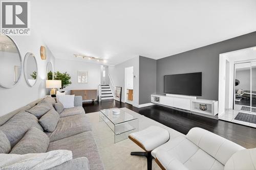 Spacious living area featuring dark wood-finish flooring, a contemporary accent wall, and recessed lighting - 19 Glen Forest Drive, Hamilton, ON 