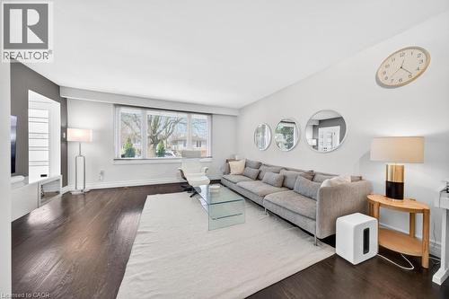 Spacious living area featuring dark wood-finish flooring, a large window providing natural light, and light-toned walls - 19 Glen Forest Drive, Hamilton, ON 
