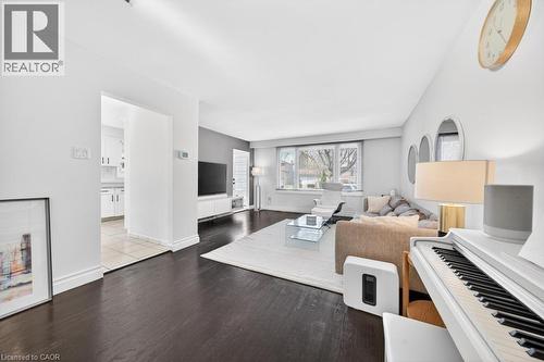 Open-concept living area featuring dark wood-finish flooring, white baseboards, and a large front-facing window - 19 Glen Forest Drive, Hamilton, ON 