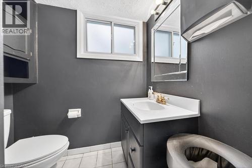 Bathroom featuring a white window, built-in medicine cabinet, dark vanity with white countertop, and tile flooring - 19 Glen Forest Drive, Hamilton, ON 